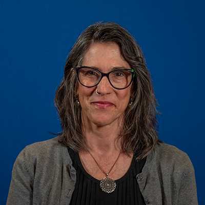 A middle-aged white woman with shoulder-length salt-and-pepper hair and glasses.
