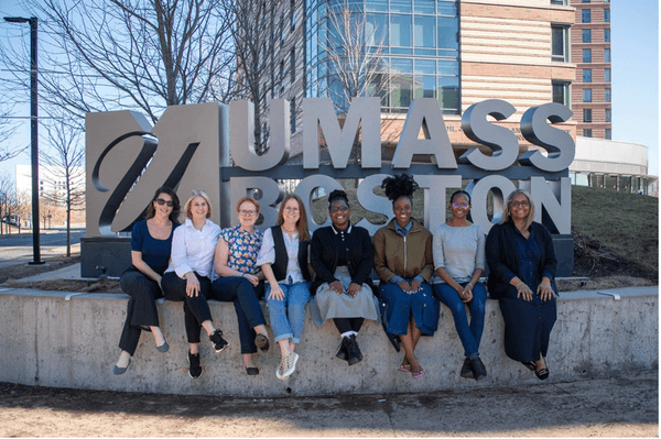 A group of ARRT fellows, mentors, and program administrators sitting outside in front of the UMass Boston sign